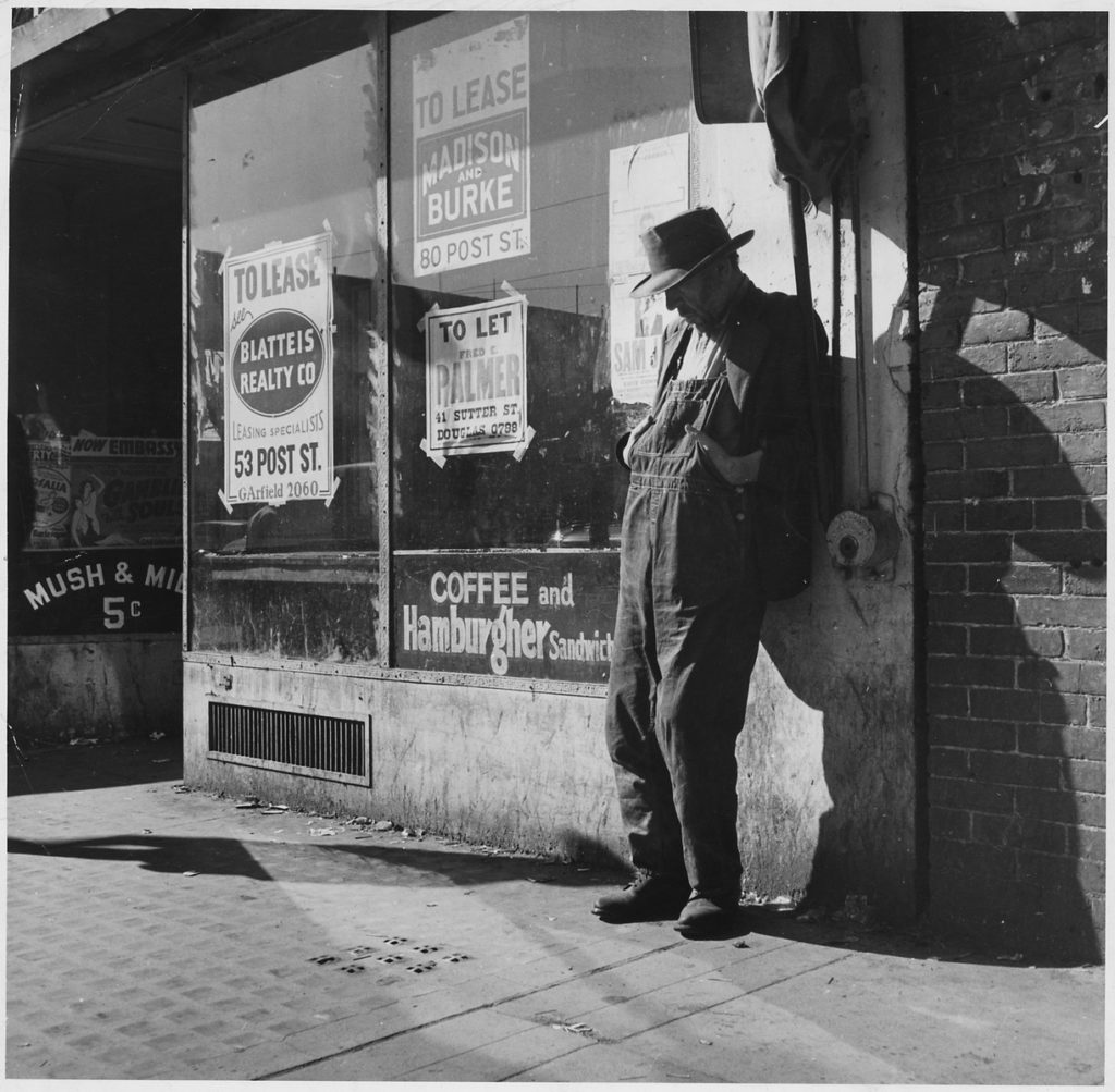 An unemployed man leaning against a building during the Great Depression, which was one of the causes of World War II.